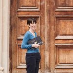 Sandrine Audegond devant une grande porte en bois, un livre sous le bras.